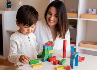 a teacher sitting with a child, encouraging him as he builds with blocks