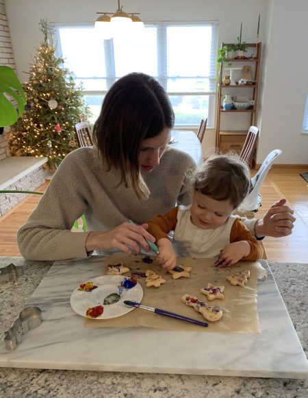 A mom, with her toddler on her lap, decorating Christmas cookies