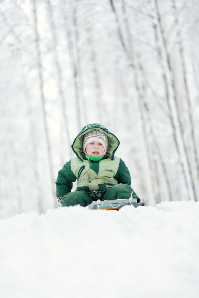 a boy on top of a hill on a sled with snow falling