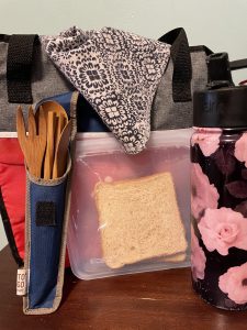 Pictured is a bamboo utensil set, Stasher sandwich bag, reusable metal water bottle, reusable lunch bag and reusable napkin