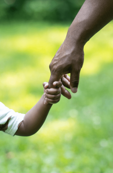 a close up of an African American boy holding his father’s hand