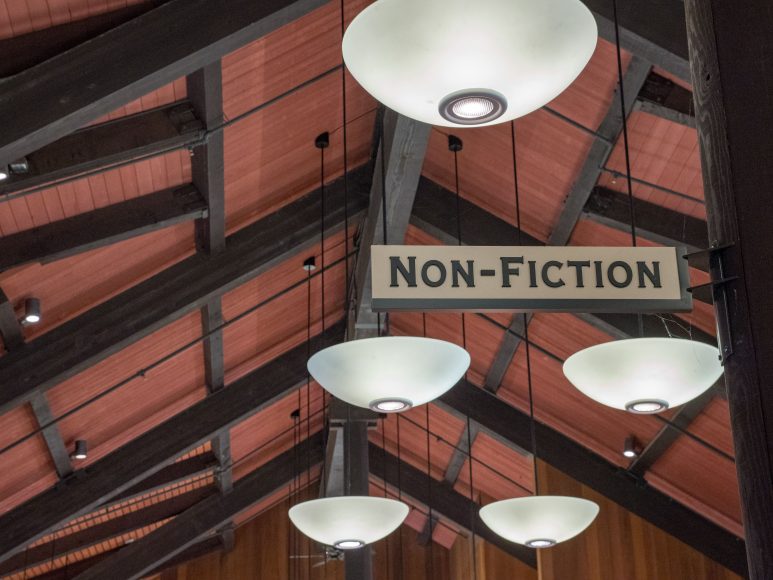 a non-fiction sign hanging from a wooden ceiling in a library