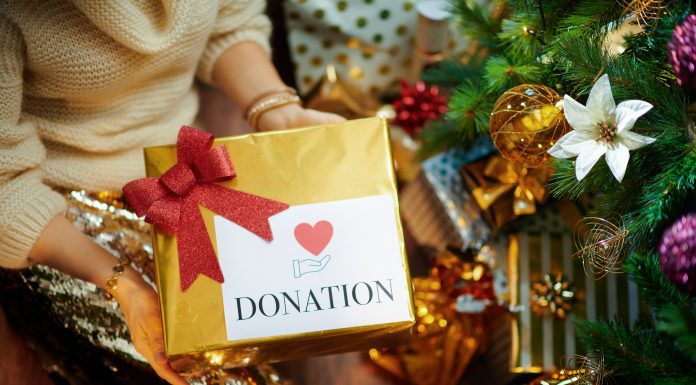 a close up of a Christmas tree as a woman puts a gift, marked “donation” underneath it