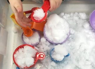 a snow sensory bin filled with snow and measuring cups