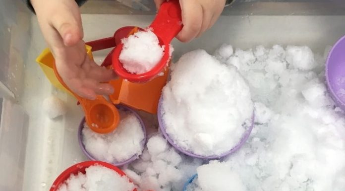 a snow sensory bin filled with snow and measuring cups