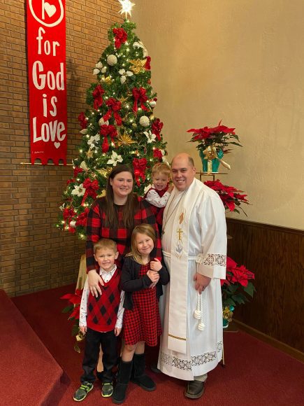 a pastor and his family standing by the Christmas tree in church