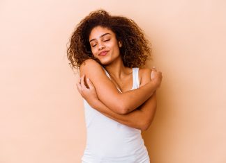 Young african american woman isolated on beige background hugs, smiling carefree and happy.