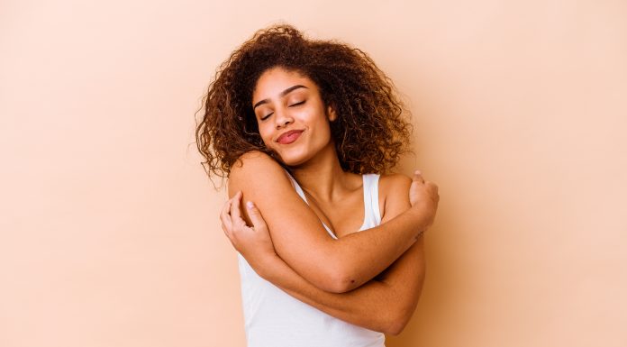 Young african american woman isolated on beige background hugs, smiling carefree and happy.