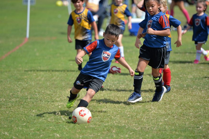 a boy in an I9 jersey kicking a soccer ball during a game