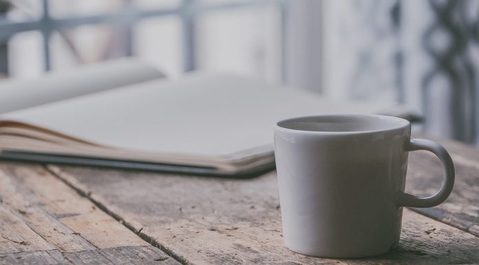 a simple white mug on a wooden table next to an open journal