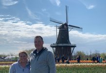 a husband and wife standing in front of a windmill in a field of tulips while on a trip to Holland, Michigan