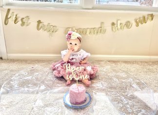 a little girl on her first birthday, dressed up as she sits in front of her birthday cake