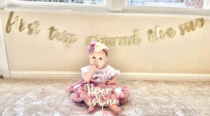 a little girl on her first birthday, dressed up as she sits in front of her birthday cake