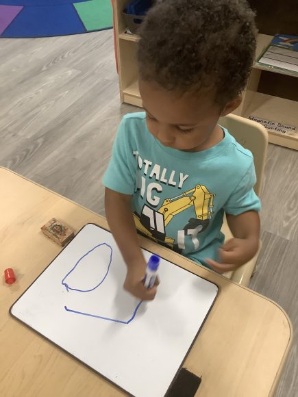 a boy practicing his letters on a white board with a dry erase marker