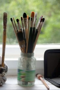 paint brushes in a glass jar on a table near a window