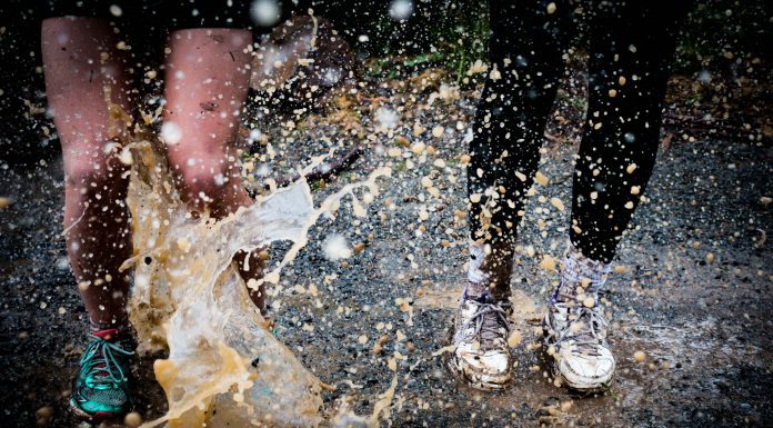 a close-up of two people jumping in a mud puddle as the mud splashes over their legs