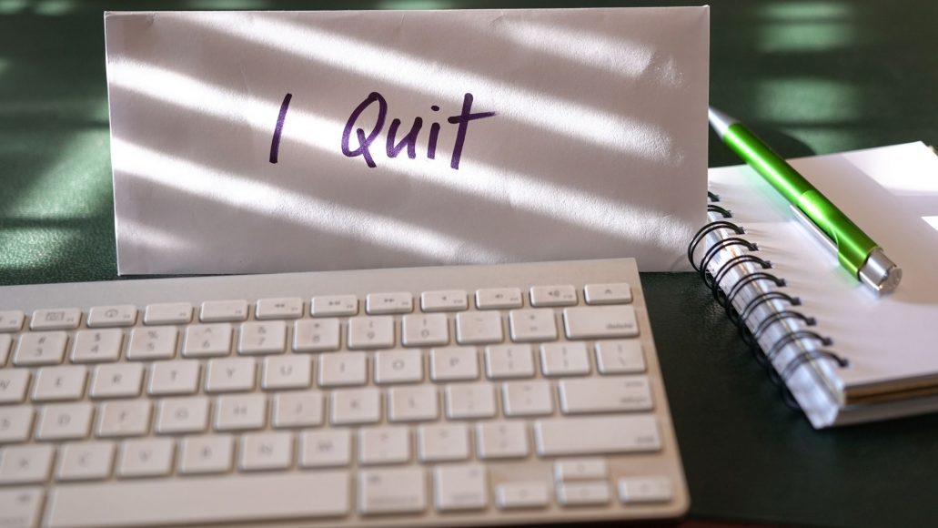 a keyboard, notebook, and pen on a desk next to a note that says, “I Quit"