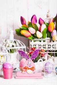 an Easter scene with a wire basket of tulips, cloth butterflies, and colorful eggs