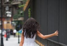 a woman walking away as she runs her hand along a metal fence