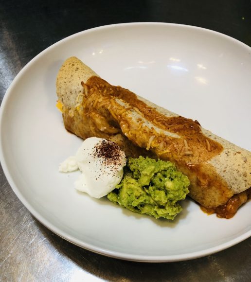 black bean and sweet potato enchilada on a plate with guacamole and sour cream
