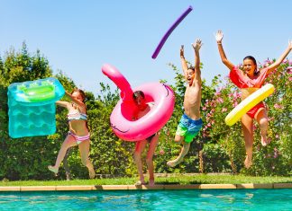 kids with pool floats and pool noodles jumping into a pool