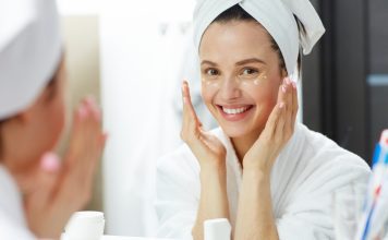 a woman in a white robe with her head wrapped in a towel as she does her daily skincare routine