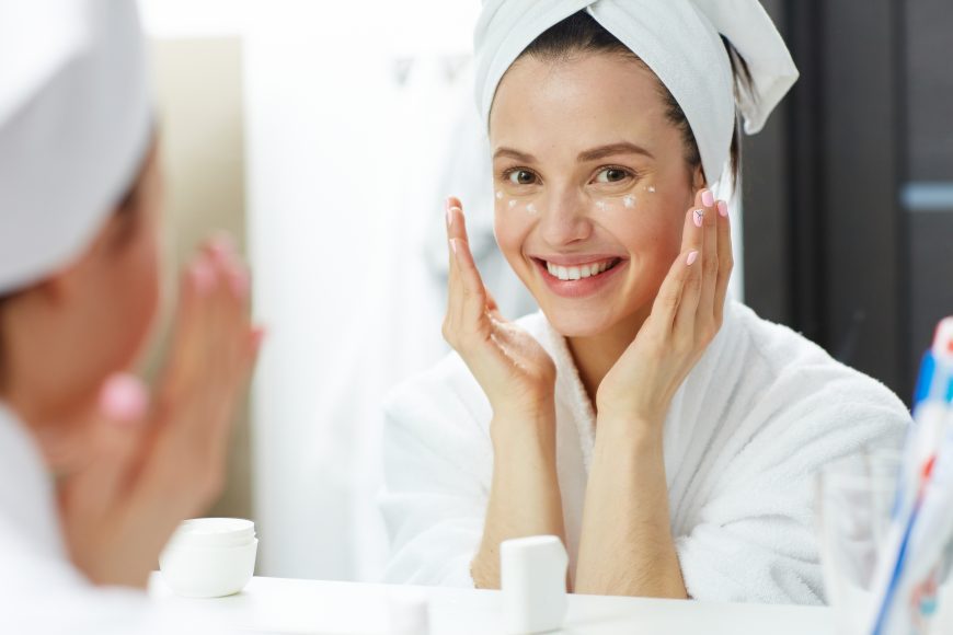 a woman in a white robe with her head wrapped in a towel as she does her daily skincare routine 