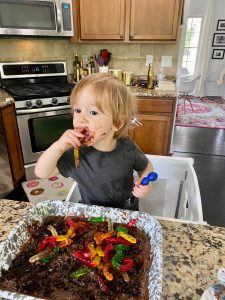 a toddler boy in front of a pan of chocolate dirt and gummy worms