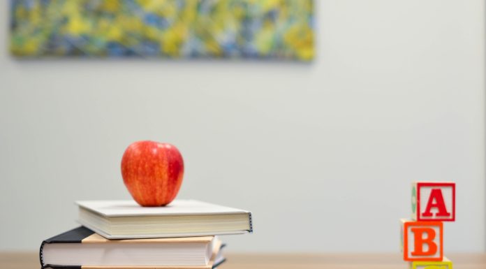 a stack of books with an apple on top that sits on a desk next to colored pencils and A, B, C blocks to represent back-to-school