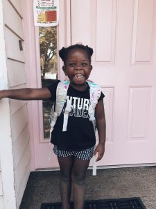 an African-American girl wearing a backpack and smiling big for her back-to-school picture