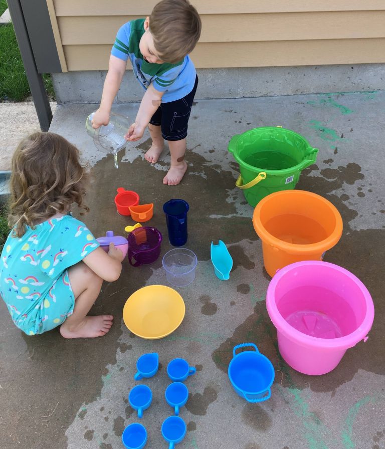 kids playing with water in the driveway as they pour and measure it into different sized and shaped containers as a science experiment