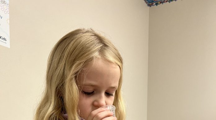 a young girl in the doctor’s office, sipping medicine from a small paper cup