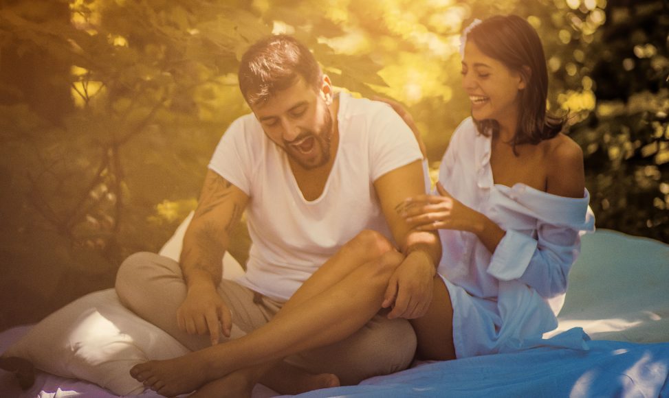 a man and a woman on a blanket in a wooded setting, laughing together