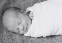 a black and white photo of a newborn baby swaddled up and sleeping with a smile on his face
