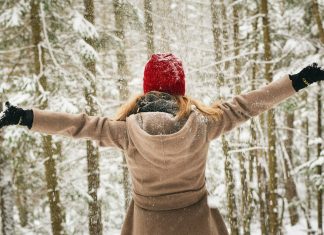 a woman standing with her arms outstretched in the woods as it is snowing