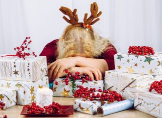 a woman wrapping holiday gifts with her head down on the table in overwhelm