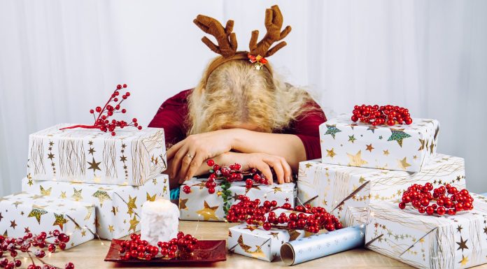 a woman wrapping holiday gifts with her head down on the table in overwhelm