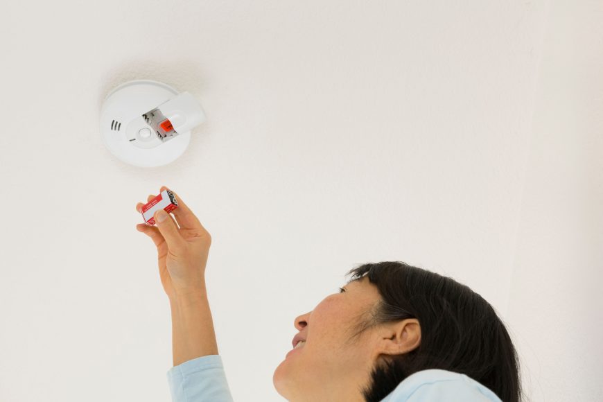 a woman changing the battery in a fire alarm
