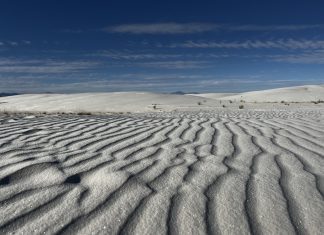wavy lines in white sand in the foreground with a blue sky in the background