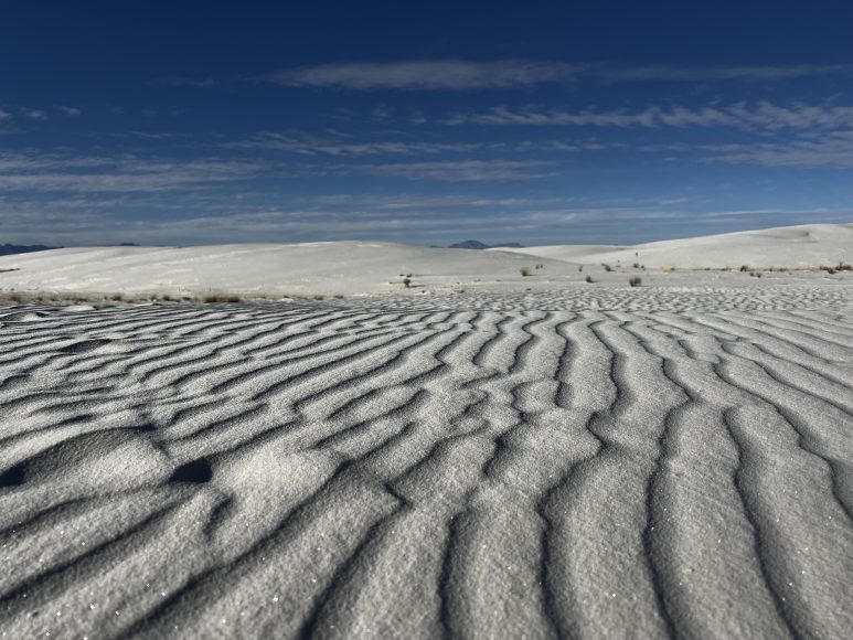wavy lines in white sand in the foreground with a blue sky in the background