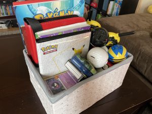 a white basket full of Pokemon books, cards, and toys