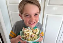a young boy holding bowl full of popcorn with a big smile on his face