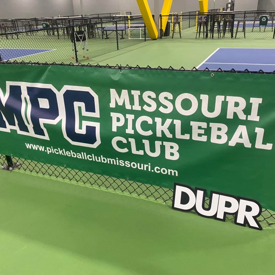 a picture of a banner on a fence in an indoor pickle ball facility that says, “Missouri Pickleball Club"