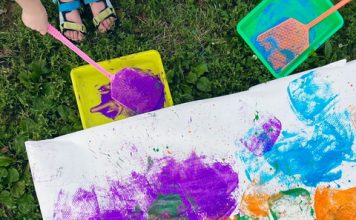 children painting on large sheets of paper outside in the grass as part of their art-making